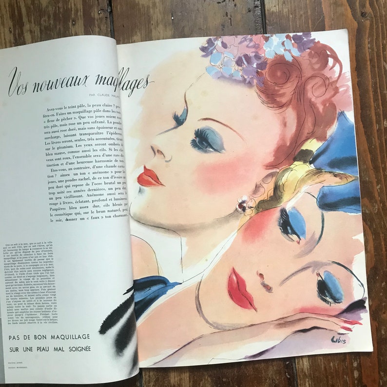 Pu&ograve; includere: Pagina di rivista vintage con un'illustrazione di moda di tre volti di donna. L'opera presenta rossetto rosso, ombretto blu e dettagli floreali. Il testo recita "Vos nouveaux maiflages" e "Pas de bon maquillage sur une peau mal soign&eacute;e."