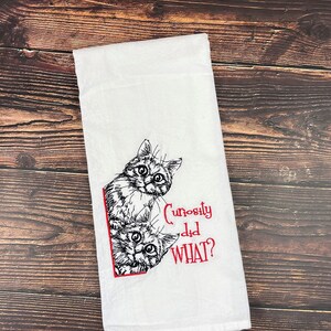 May include: White kitchen towel with a black and white illustration of two cats peeking around a corner. The text "Curiosity did WHAT?" is embroidered in red.