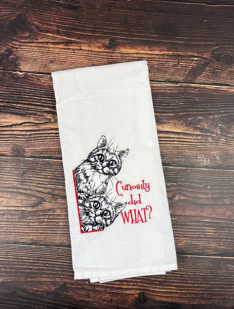 May include: White kitchen towel with a black and white illustration of two cats peeking around a corner. The text "Curiosity did WHAT?" is embroidered in red.
