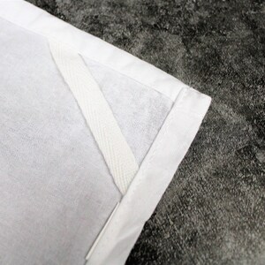 May include: Close-up of a white fabric with a white seam tape sewn along the edge.