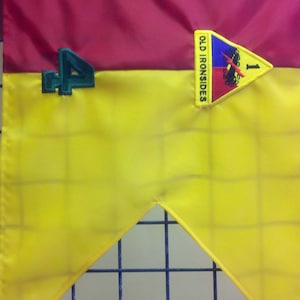 Op de afbeelding: Een gele en rode vlag met een groen nummer "4" en een patch met de tekst "Old Ironsides" met een blauw, rood en wit ontwerp en een nummer "1" in het midden.