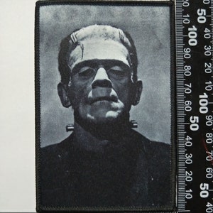 Pu&ograve; includere: Immagine in bianco e nero del mostro di Frankenstein su una toppa di tessuto nero. La toppa misura circa 10 cm per 12,5 cm.