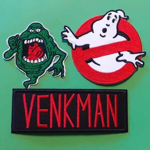 May include: Three embroidered patches featuring the Ghostbusters logo, a green ghost, and the name "VENKMAN" in red lettering on a black background.