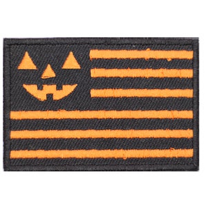Puede incluir: Un parche bordado en negro y naranja con una cara de calabaza y un diseño de bandera estadounidense.