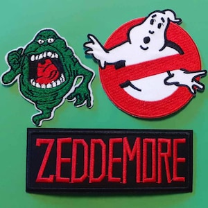 Puede incluir: Tres parches bordados con personajes de la película Ghostbusters. Los parches son verdes, blancos y rojos. El texto "ZEDDEMORE" está en un parche negro.