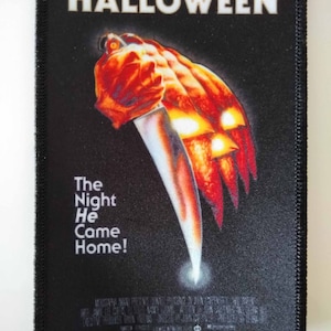 May include: A black and red Halloween patch with the text "HALLOWEEN" and "The Night He Came Home!"  The patch features a knife and a pumpkin with a menacing face.