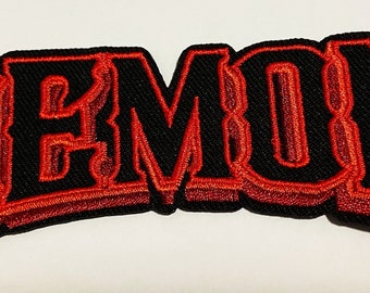 Op de afbeelding: Rode geborduurde patch met het woord "DEMON" in een vet, 3D-stijl lettertype. De letters zijn zwart omrand en rood gevuld.