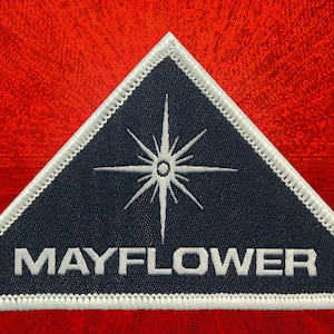 May include: A white embroidered patch with a blue triangle and a white star in the center. The text "MAYFLOWER" is written in white below the star.