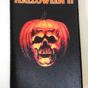 Op de afbeelding: Een zwarte en oranje Halloween III-patch met een jack-o'-lantern met een schedelgezicht.
