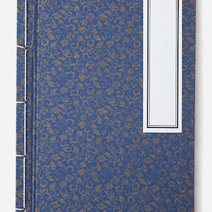 May include: A blue book with a gold floral pattern and gold corner accents. The book has a white label with a black border.