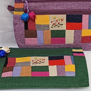 May include: Two patchwork fabric zippered pouches with floral embroidery. The larger pouch is purple with a green, yellow, red, and brown patchwork design. The smaller pouch is green with a similar patchwork design.