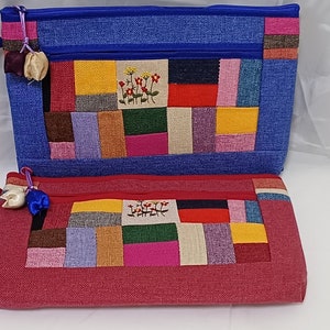 以下が含まれることがあります： カラフルなパッチワークのデザインが施されたファスナー付きの布製ポーチが2つ。上のポーチは青で、青いファスナーが付いています。下のポーチは赤で、赤いファスナーが付いています。両方のポーチには、小さな布の花の装飾が付いています。