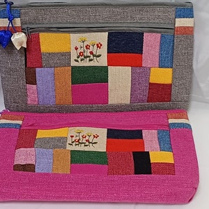 Op de afbeelding: Twee stoffen tasjes met kleurrijke patchwork-ontwerpen en geborduurde bloemen. De tasjes hebben ritsen en zijn versierd met blauwe en witte lintjes.