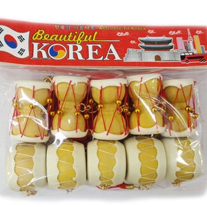 May include: A set of eight small, wooden, hand drums with red string and gold beads. The drums are packaged in a clear plastic bag with a red and white label that says "Beautiful Korea" and features a Korean flag and a drawing of a traditional Korean building.