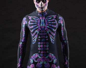 May include: A person wearing a black skeleton costume with purple and blue floral details. The costume is a full-body suit with a zipper in the front. The person has a sugar skull makeup design on their face.