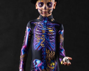 May include: A child dressed in a black skeleton costume with purple and gold accents. The costume features a skull and flames design. The child is wearing a black top hat and holding a small white skull.