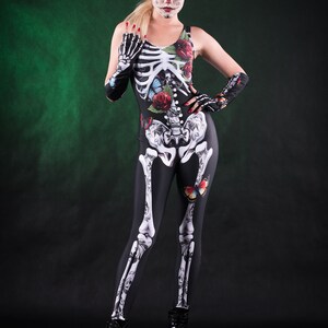 May include: A woman wearing a black skeleton costume with floral and butterfly accents. She has red flowers in her hair and white face paint with black accents.