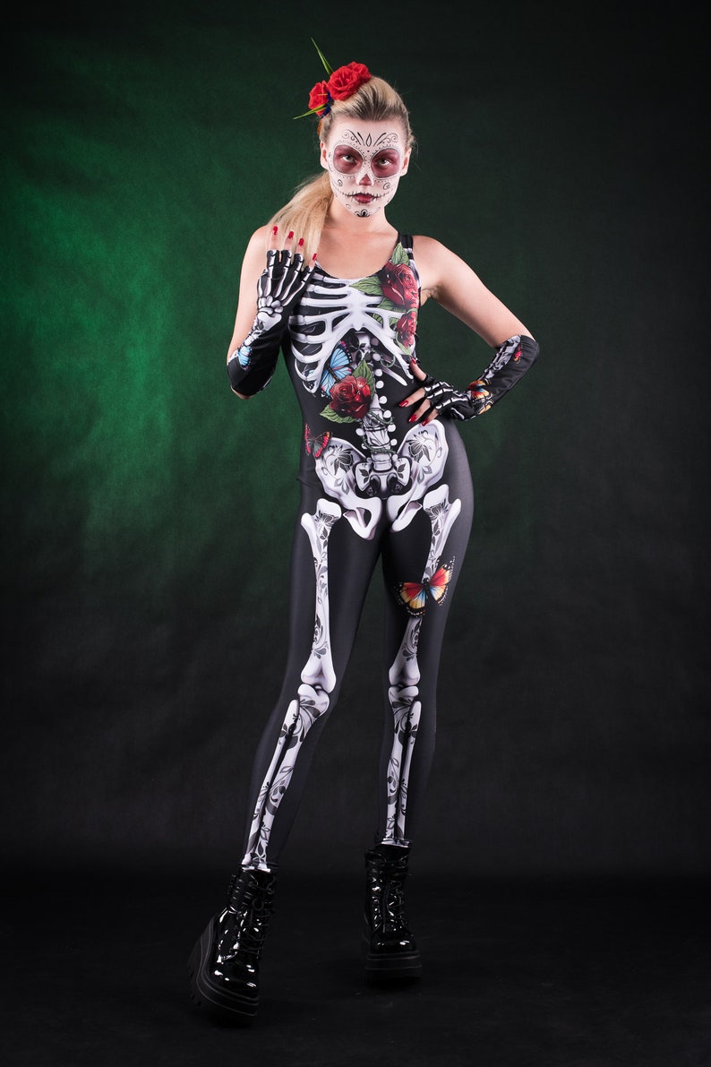 May include: A woman wearing a black skeleton costume with floral and butterfly accents. She has red flowers in her hair and white face paint with black accents.