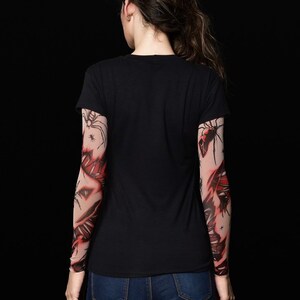 May include: A person wearing a black t-shirt with red and black spider web tattoo sleeves.