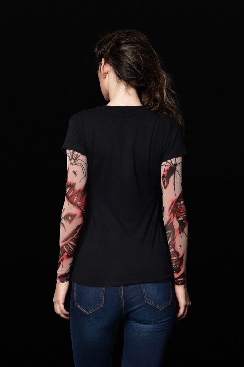 May include: A person wearing a black t-shirt with red and black spider web tattoo sleeves.