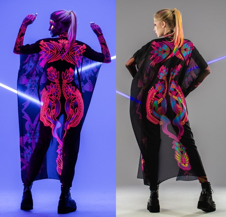 Pode incluir: Duas mulheres vestindo t&uacute;nicas pretas transparentes com padr&otilde;es florais coloridos em neon. As t&uacute;nicas s&atilde;o longas e fluidas, e as mulheres usam cal&ccedil;as pretas e botas.