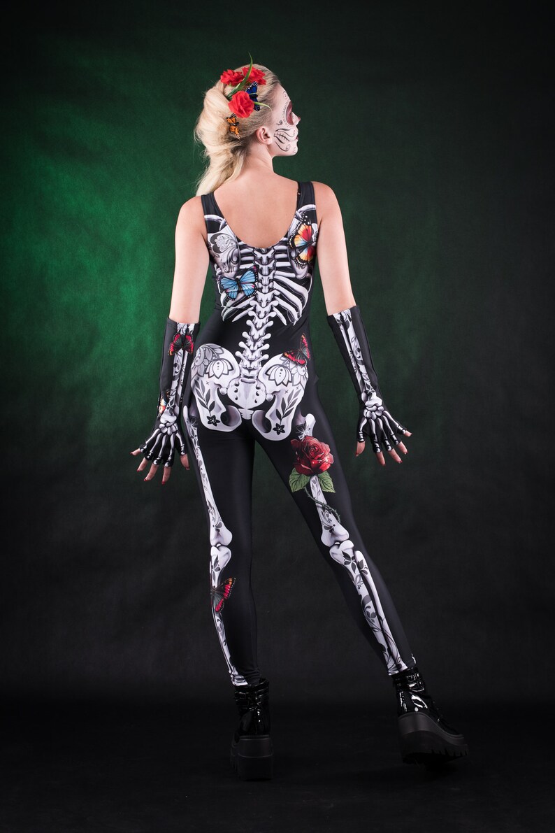 May include: A woman wearing a black skeleton costume with butterflies and roses. The costume is a full-body jumpsuit with a skeleton design and floral accents.