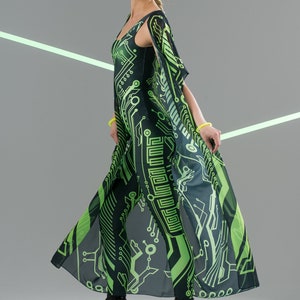 May include: A woman wearing a black and green jumpsuit with a circuit board pattern. She is wearing black platform boots and has green makeup on her face.