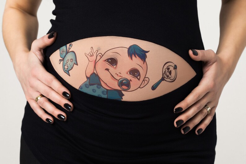 K&ouml;nnte beinhalten: Ein schwarzes Umstandsoberteil mit einem Baby-Motiv. Die Grafik zeigt ein Cartoon-Baby mit Schnuller, blauem Irokesenschnitt und Totenkopf-Rassel. Eine blaue geisterhafte Figur ist ebenfalls enthalten.