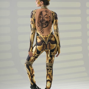 May include: A woman wearing a black and gold jumpsuit with a graphic print of a face on the back. She is wearing black platform boots.