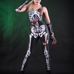 May include: A woman wearing a black skeleton costume with red roses and butterflies. She has a sugar skull makeup design and is wearing black platform shoes.