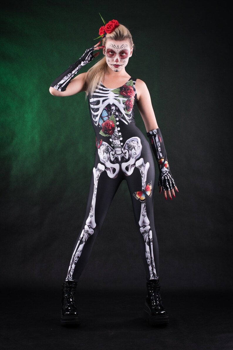 May include: A woman wearing a black skeleton costume with red roses and butterflies. She has a sugar skull makeup design and is wearing black platform shoes.