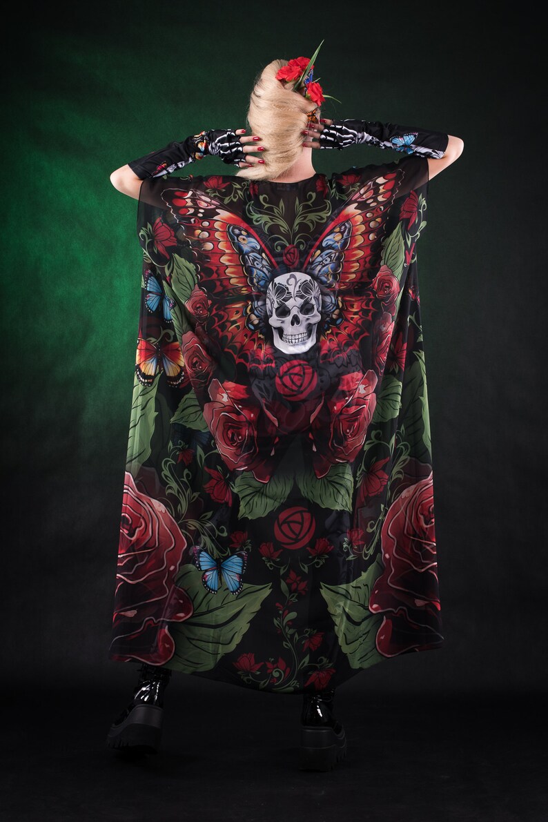 May include: A black sheer maxi dress with a skull and butterfly print. The dress features red roses, green leaves, and a skull with a butterfly on its head. The dress is worn by a person with blonde hair and a flower crown.