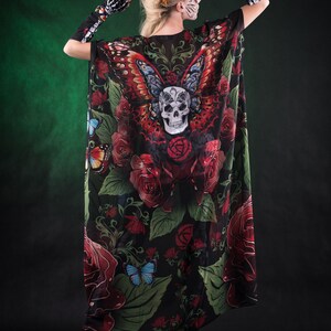 May include: A black sheer cape with a skull and butterfly design. The cape features red roses, green leaves, and colorful butterflies. The cape is worn by a person with a skull face paint and red flowers in their hair.