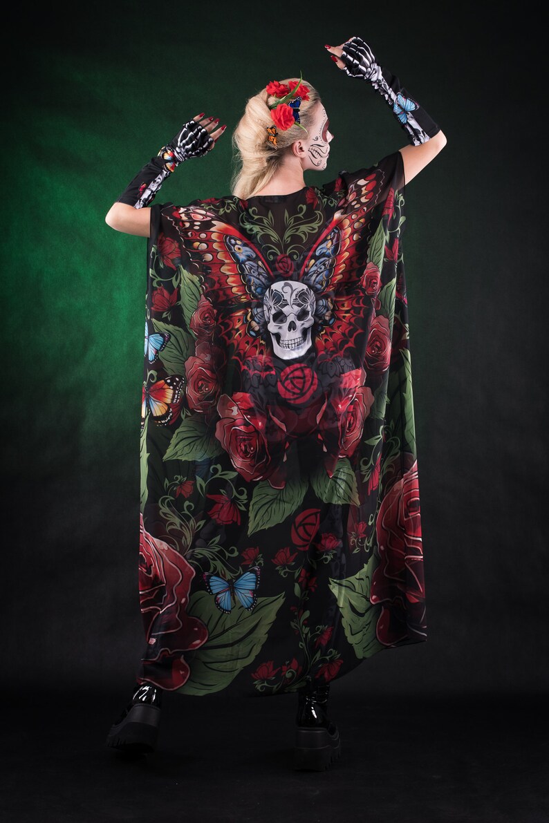 May include: A black sheer cape with a skull and butterfly design. The cape features red roses, green leaves, and colorful butterflies. The cape is worn by a person with a skull face paint and red flowers in their hair.