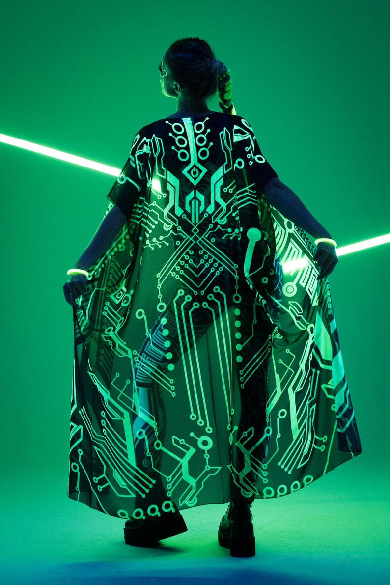 May include: A person wearing a black sheer kimono with a green circuit board pattern. The kimono is glowing under a green light.
