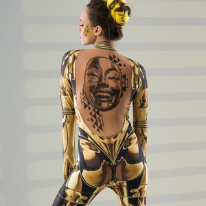 May include: A woman wearing a gold and black jumpsuit with a geometric pattern and a face tattoo on her back.