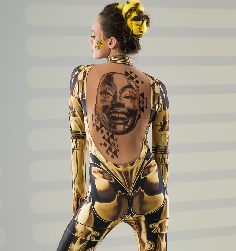 May include: A woman wearing a gold and black jumpsuit with a geometric pattern and a face tattoo on her back.