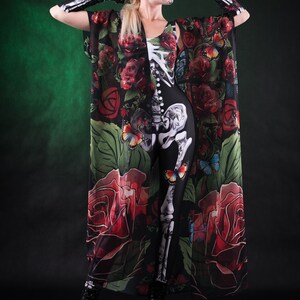 May include: A woman wearing a black skeleton bodysuit with a sheer floral print kimono. The kimono has red roses, green leaves, and butterflies. She is wearing black boots and has a sugar skull makeup design on her face.