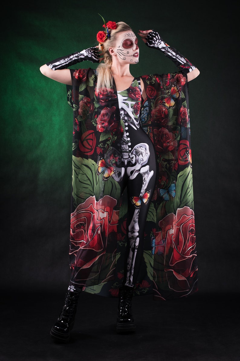 May include: A woman wearing a black skeleton bodysuit with a sheer floral print kimono. The kimono has red roses, green leaves, and butterflies. She is wearing black boots and has a sugar skull makeup design on her face.