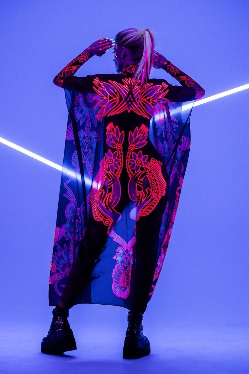 Pode incluir: Um top preto transparente com um design floral rosa e roxo. O top &eacute; usado sobre um body preto. A modelo est&aacute; usando botas de plataforma pretas.