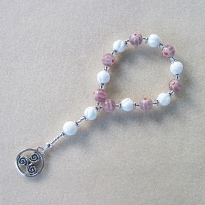 May include: A white and pink beaded bracelet with a silver charm featuring a triple spiral design.