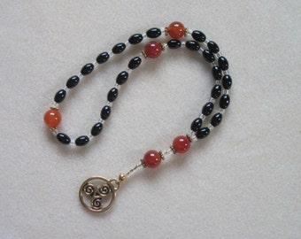 Anglican Rosary – Black Glass ovals, Fire Agate, and a Gold finished Celtic Triskele (Trinity) pendant.