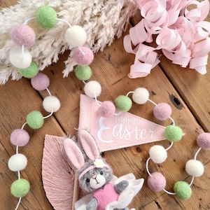 May include: A pink and green felt ball garland with a pink banner that says "Happy Easter".
