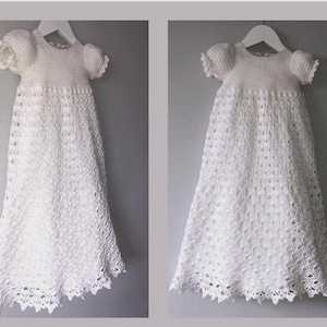 Puede incluir: Un vestido de bebé blanco de ganchillo con un diseño de encaje y mangas abullonadas.