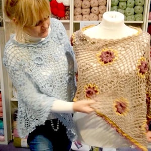 Peut inclure: Deux châles en crochet, l'un bleu clair et l'autre beige avec des accents jaunes et roses. Les châles sont exposés sur un mannequin et une personne tient le châle beige.