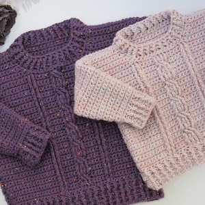 May include: Two crocheted sweaters, one purple and one pink, with a cable knit pattern.