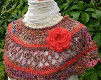 May include: A crocheted shawl in shades of brown, pink, and red with a large red crocheted flower accent. The shawl is displayed on a white mannequin.