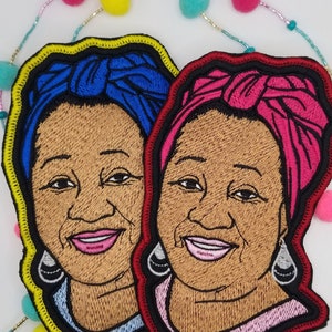 May include: Two embroidered patches featuring portraits of women with headscarves. The woman on the left has a blue headscarf and the woman on the right has a pink headscarf. Both patches have yellow and red outlines.
