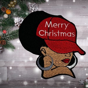 May include: Embroidered patch featuring a woman with a red baseball cap that says "Merry Christmas". The woman has brown skin, black hair, and large hoop earrings.