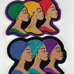 May include: Embroidered patches featuring profiles of women wearing colorful head wraps and gold hoop earrings. The patches have a black border with a purple outline. The women's skin tones are brown, and the head wraps are green, yellow, red, blue, teal, and purple.